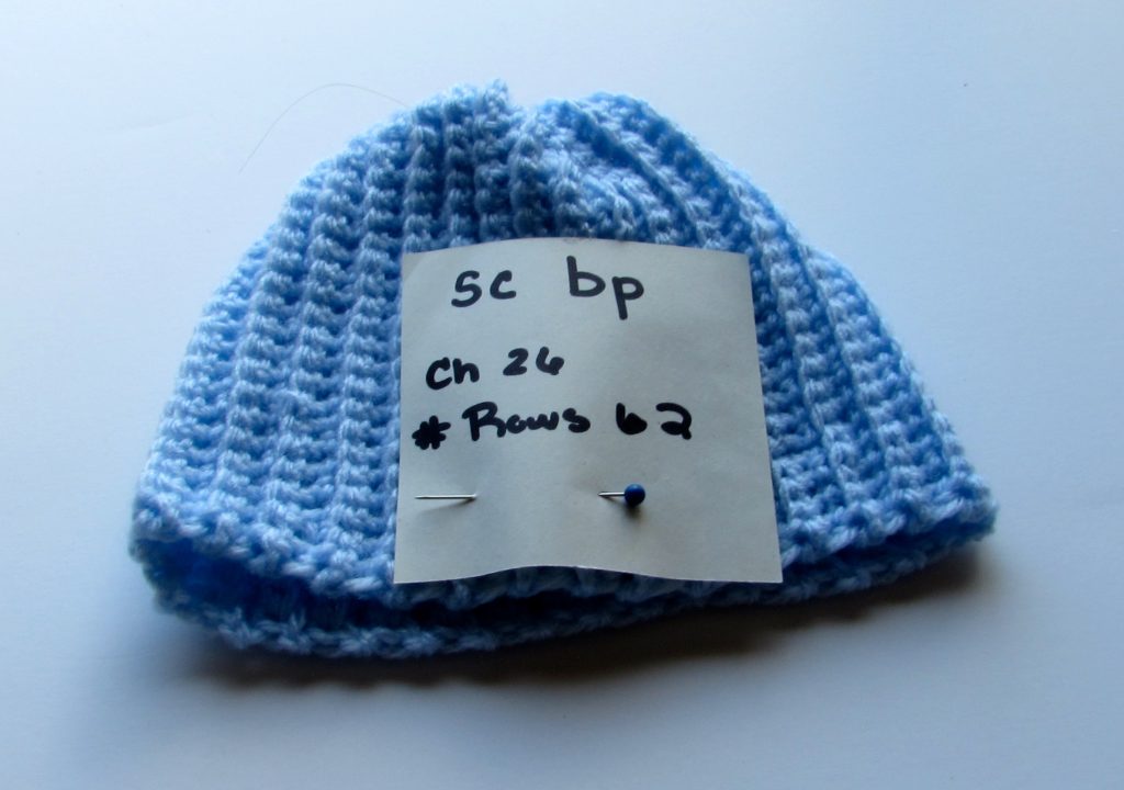 crochet beanie with a note pinned to it that says what stitch was used, the number of chains in the foundation chain, and the row the project was left off at.