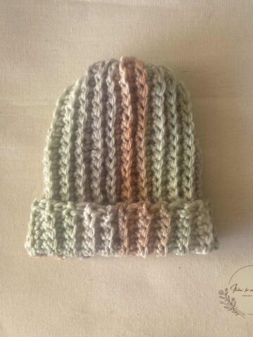 Striped ribbed crochet baby beanie in soft green, cream, and brown yarn with a folded brim.