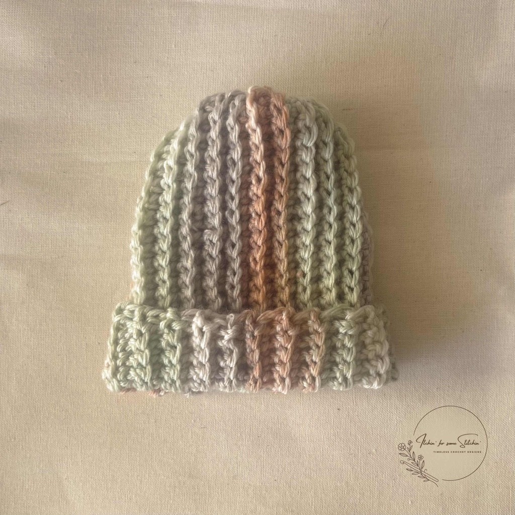 Striped ribbed crochet baby beanie in soft green, cream, and brown yarn with a folded brim.