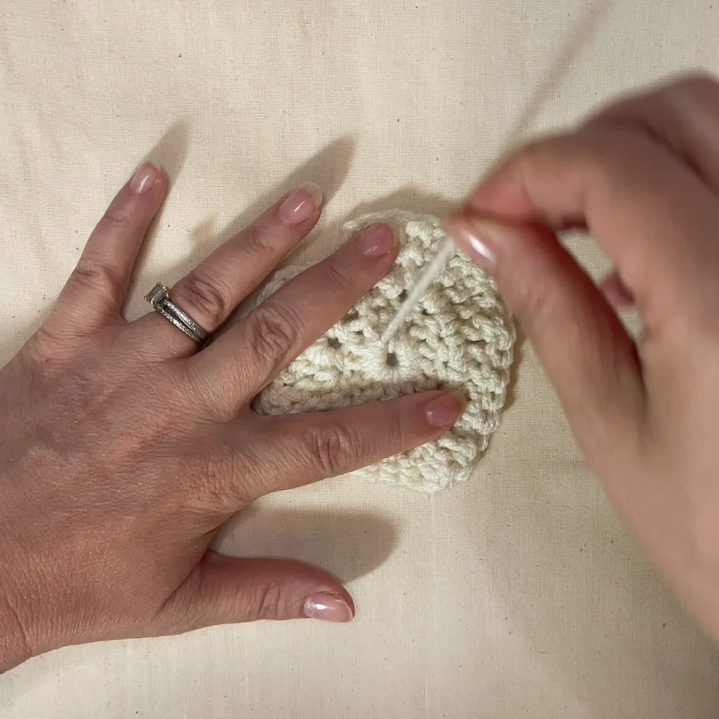 Hand pulling yarn tail through center of crochet heart to close the magic ring after finishing the pattern.