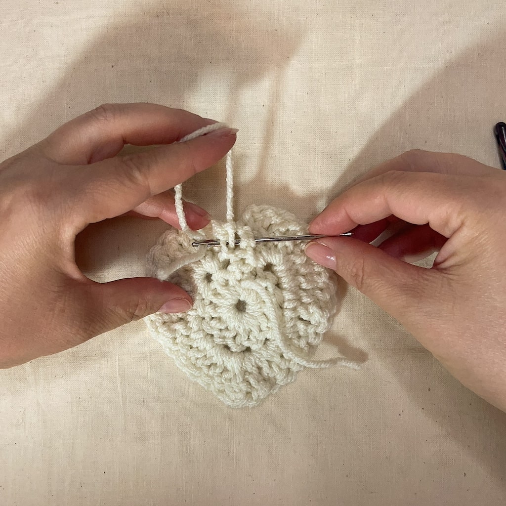 Close-up of yarn needle weaving through the top stitches of a crochet heart to close the center hole.