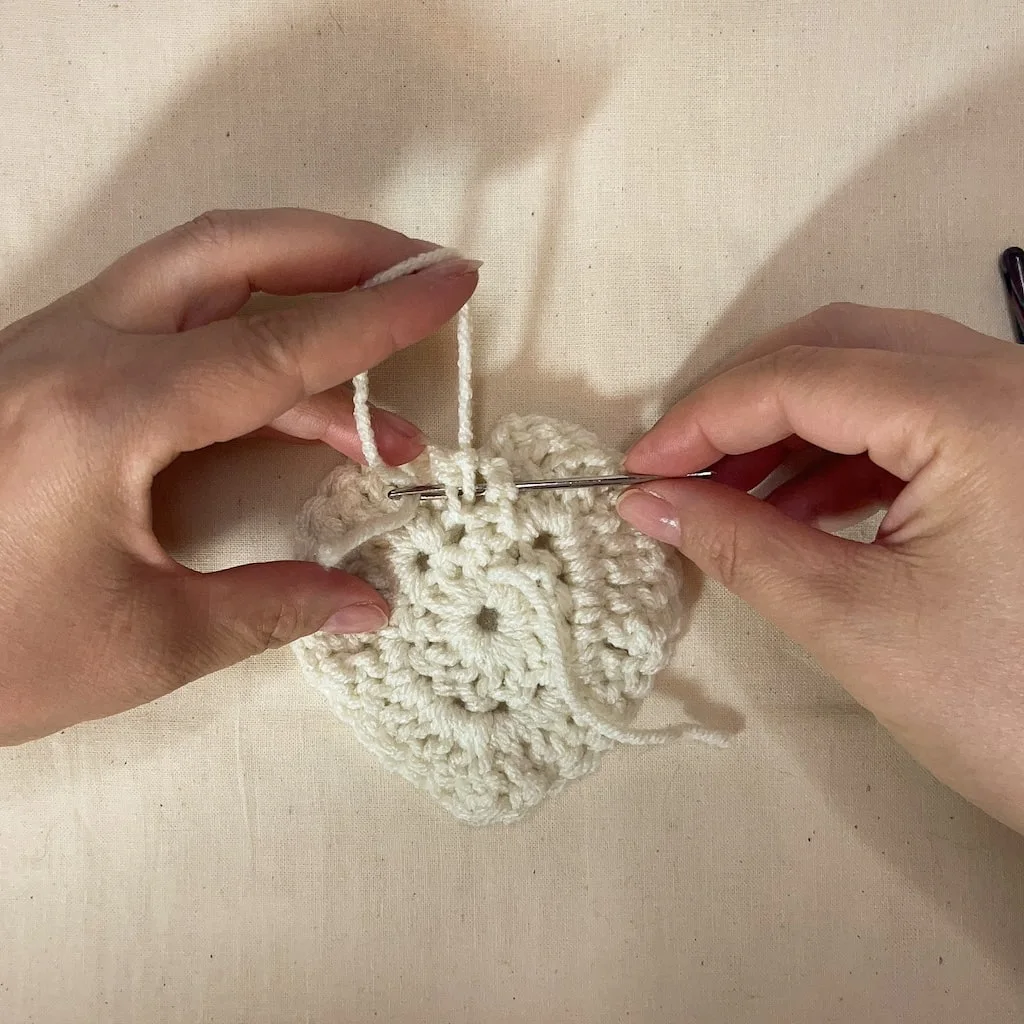 Close-up of yarn needle weaving through the top stitches of a crochet heart to close the center hole.