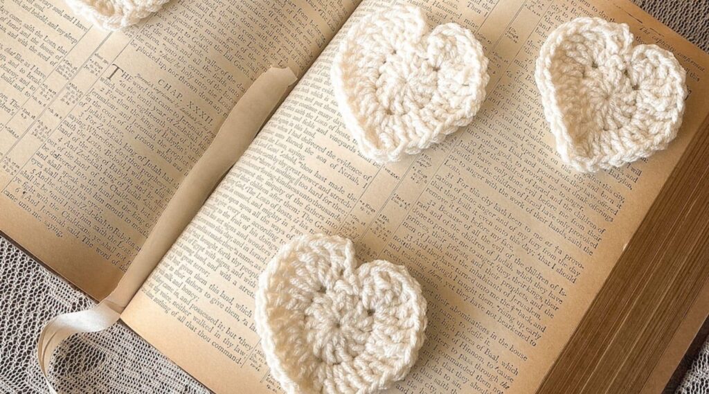 Cream lace hearts on vintage book with lace doily - hero image for free crochet pattern.