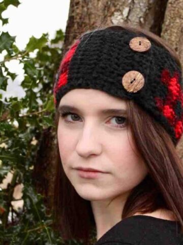 Buffalo Plaid Ear Warmer Crochet Pattern worn by a woman outdoors featuring classic red and black plaid crochet and decorative wooden buttons.