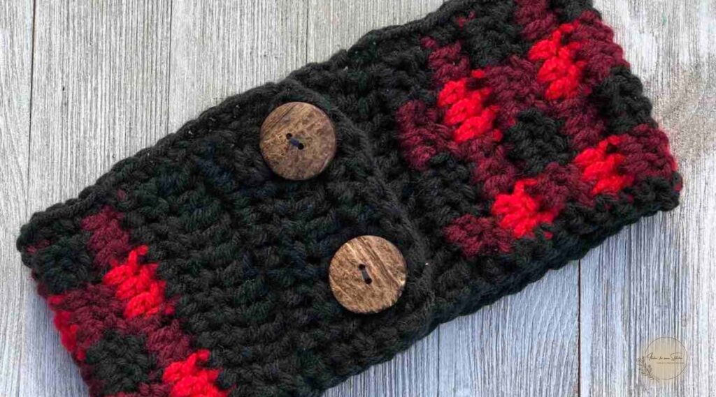 Buffalo plaid crochet ear warmer pattern worked in red, burgundy, and black yarn with decorative wooden button accents.