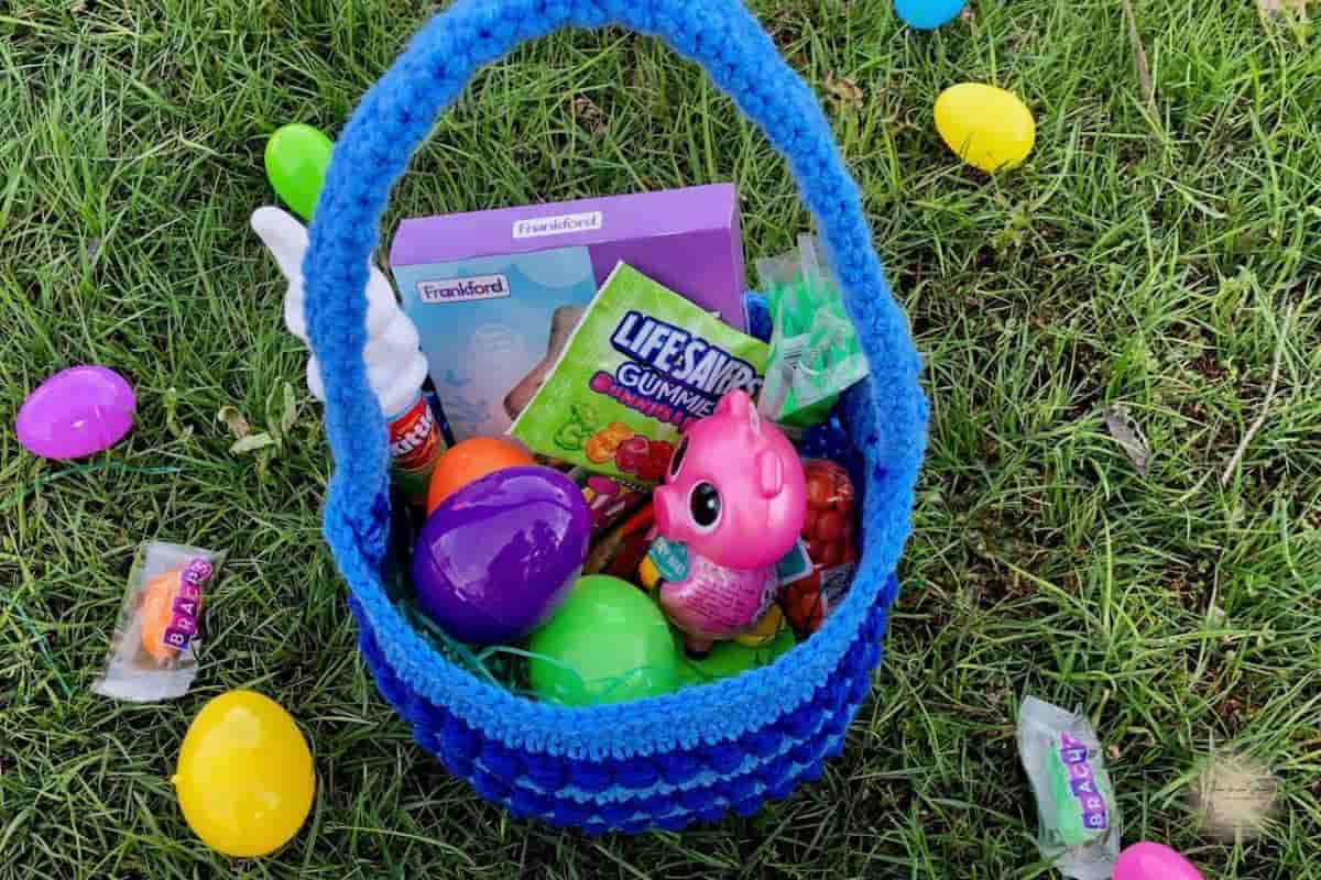 top view of a blue crochet Easter basket filled with colorful plastic eggs sitting on grass