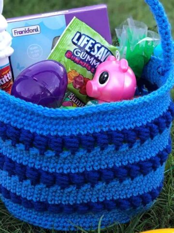 blue crochet Easter basket filled with colorful plastic eggs sitting on grass