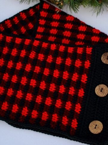 Buffalo Plaid crochet cowl with decorative wooden buttons displayed on a white background with evergreen accents.