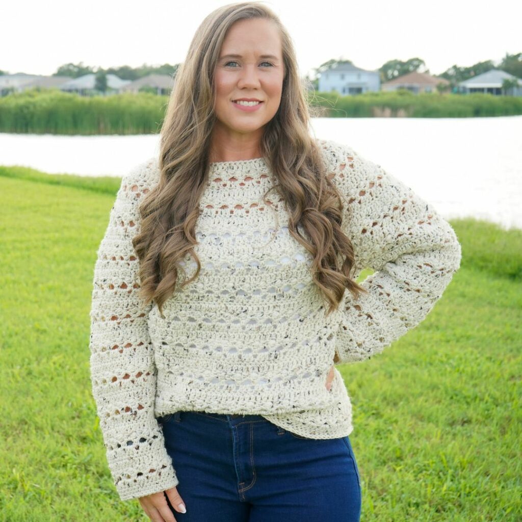 Woman wearing a cream textured crochet pullover sweater with a circular yoke and long sleeves.