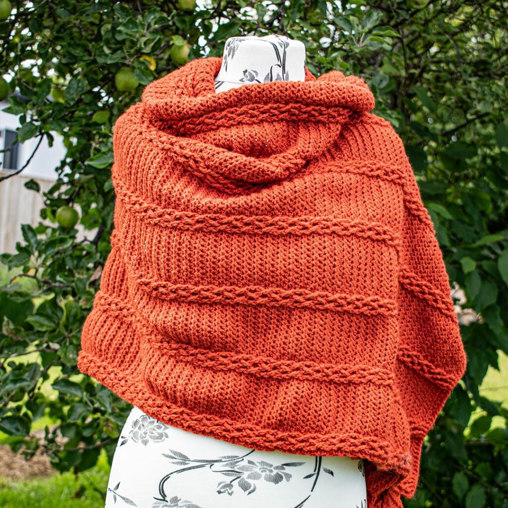 Woman wearing a rust orange crochet wrap featuring raised cable details and textured panels.
