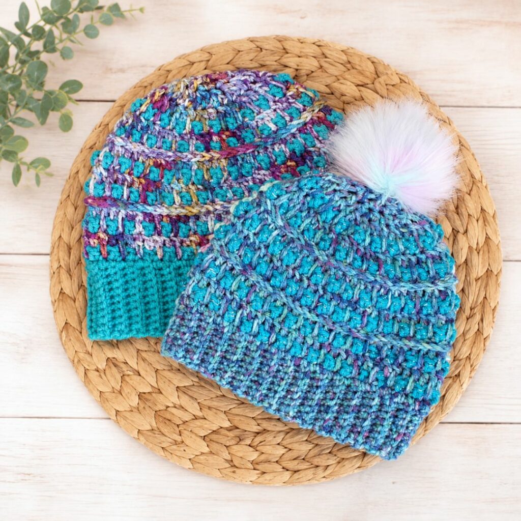 Blue and purple textured crochet beanie with a ribbed brim and fluffy white pom pom.