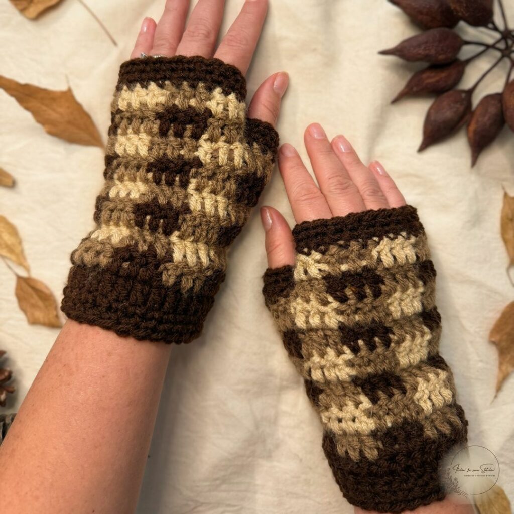 Hands wearing brown, taupe, and cream buffalo plaid crochet fingerless mitts with dark brown trim.