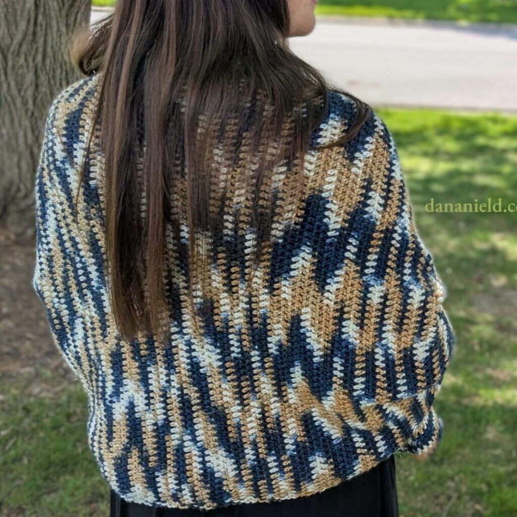 Woman wearing a blue, cream, and tan variegated crochet prayer shawl draped around her shoulders.