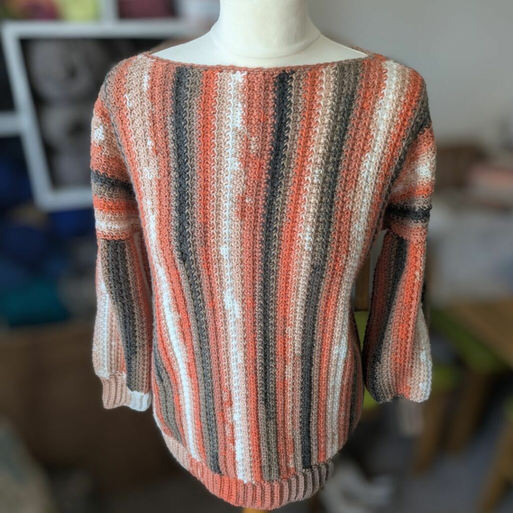 Woman wearing a relaxed crochet pullover sweater with long sleeves, ribbed cuffs and hem, and a wide boat neckline.
