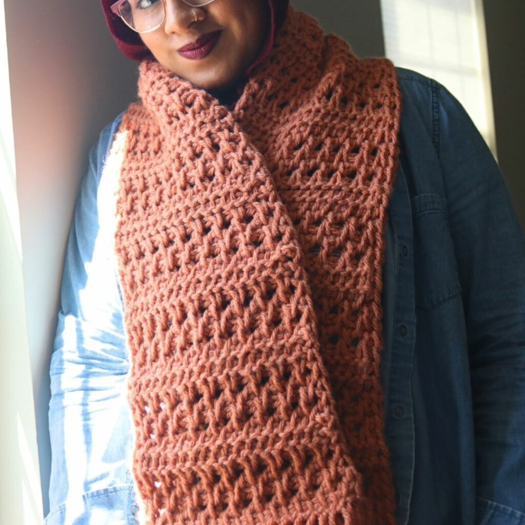 Woman wearing a textured rust-colored Tunisian crochet scarf.