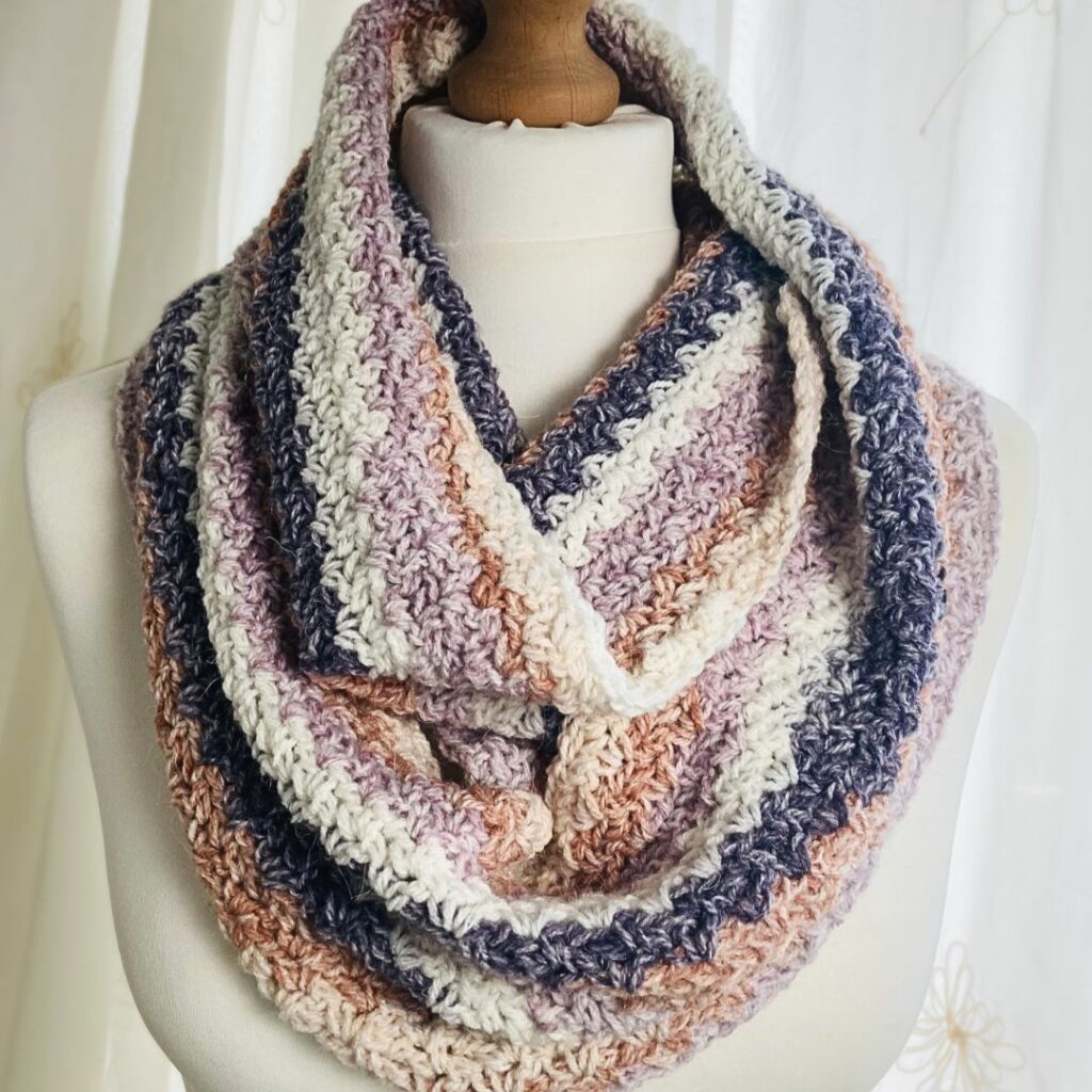 Wattlewood crochet infinity scarf with textured stripes in soft cream, pink, peach, and purple, designed by Lullaby Lodge Designs.