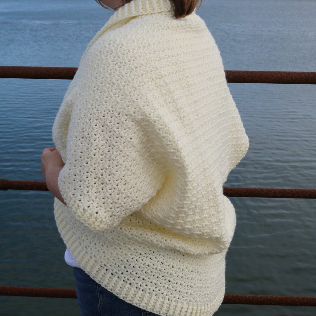 Woman wearing a cream textured crochet cocoon cardigan with an open front and ribbed edging.