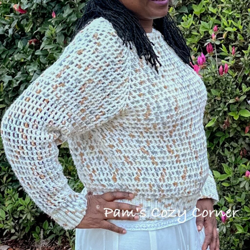 Woman wearing a cream openwork crochet sweater with long sleeves and ribbed cuffs and hem.