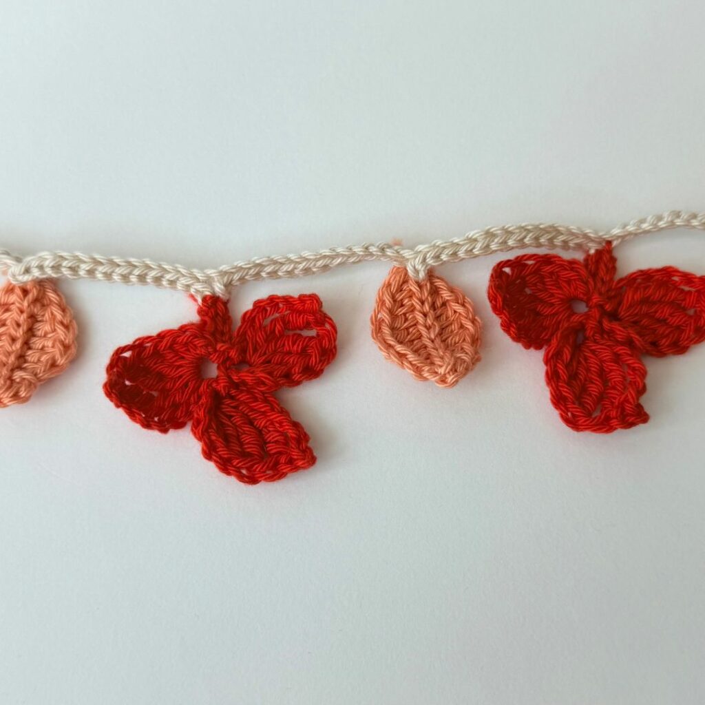 Crochet autumn leaf garland with orange leaves and red three-leaf clusters on a light brown chain.