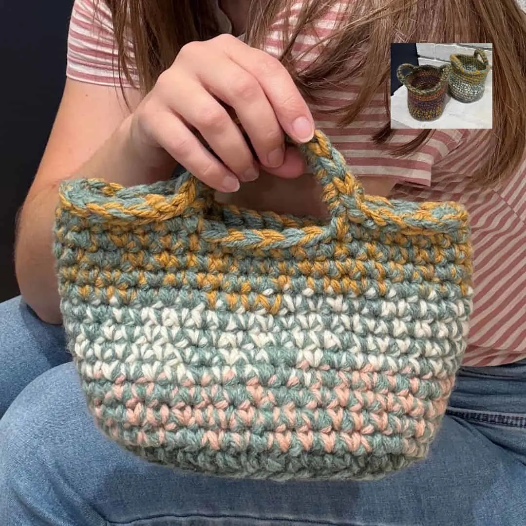 A woman wearing a pink and white striped shirt and jeans holds a small, sturdy crochet basket with built-in handles. The basket features thick, textured stitches in muted pastel shades of sage green, cream, blush pink, and mustard yellow. In the top right corner, a smaller inset image shows two additional crochet baskets in different color combinations placed on a white surface against a dark background.