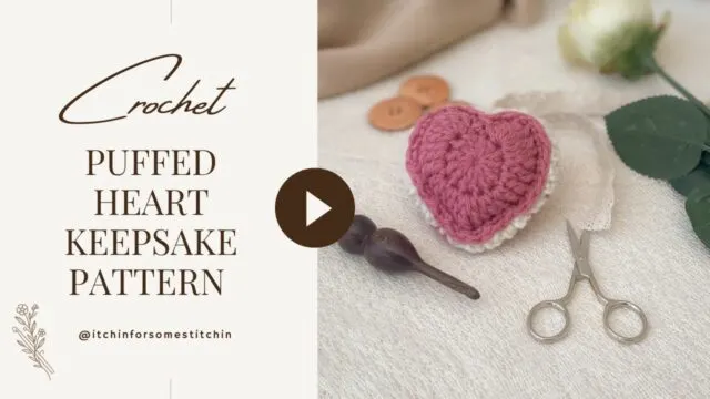 Soft vintage-style thumbnail showing a pink crochet puffed heart keepsake with lace, scissors, wooden crochet hook, and white rose on a neutral fabric background. Text reads 'Crochet Puffed Heart Keepsake Pattern' in elegant serif font.
