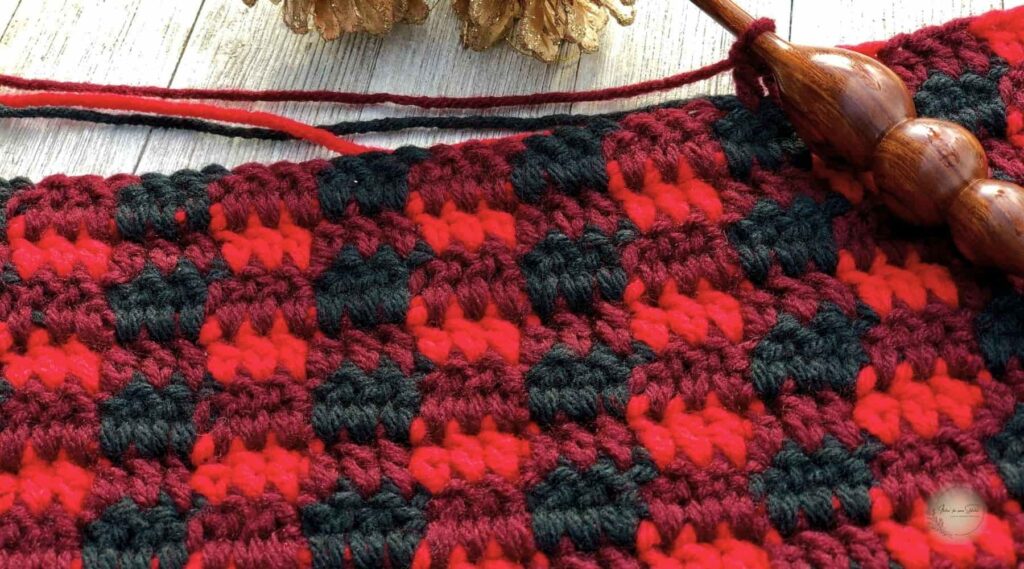 Close-up of a crochet plaid stitch swatch worked in buffalo plaid colors with a crochet hook and carried yarn.