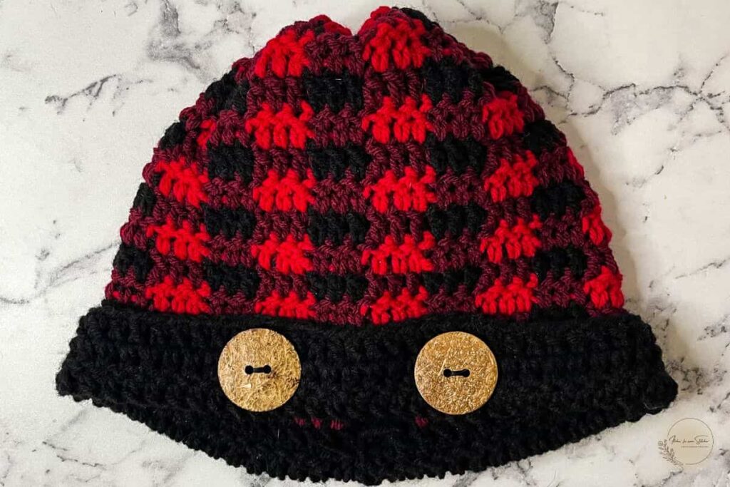 Plaid crochet beanie pattern featuring a finished buffalo plaid beanie with a folded black brim and decorative wooden buttons.