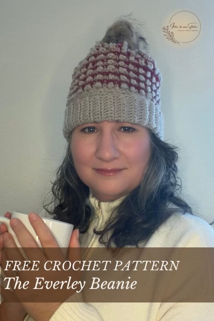 Woman wearing the Everley Beanie, a burgundy and oatmeal crochet hat with a folded ribbed brim and faux-fur pom-pom. Graphic reads &ldquo;Free Crochet Pattern: The Everley Beanie.&rdquo;